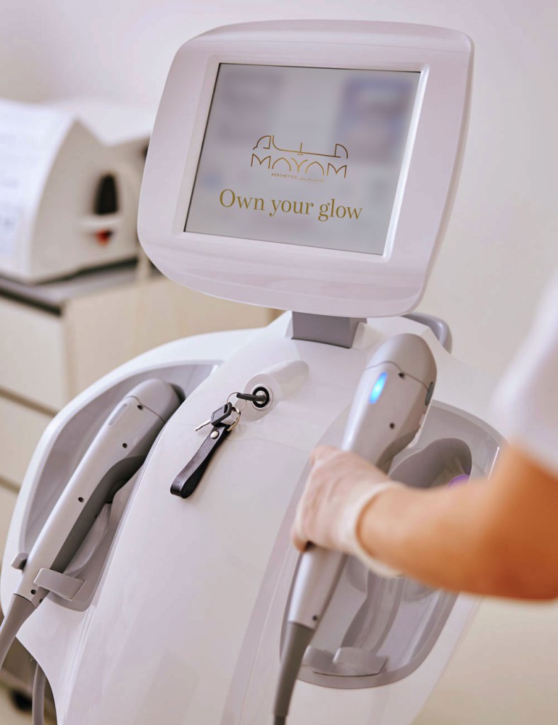 Advanced aesthetic treatment machine at Mayam Aesthetics clinic with a glowing screen displaying 'Own your glow' message.
